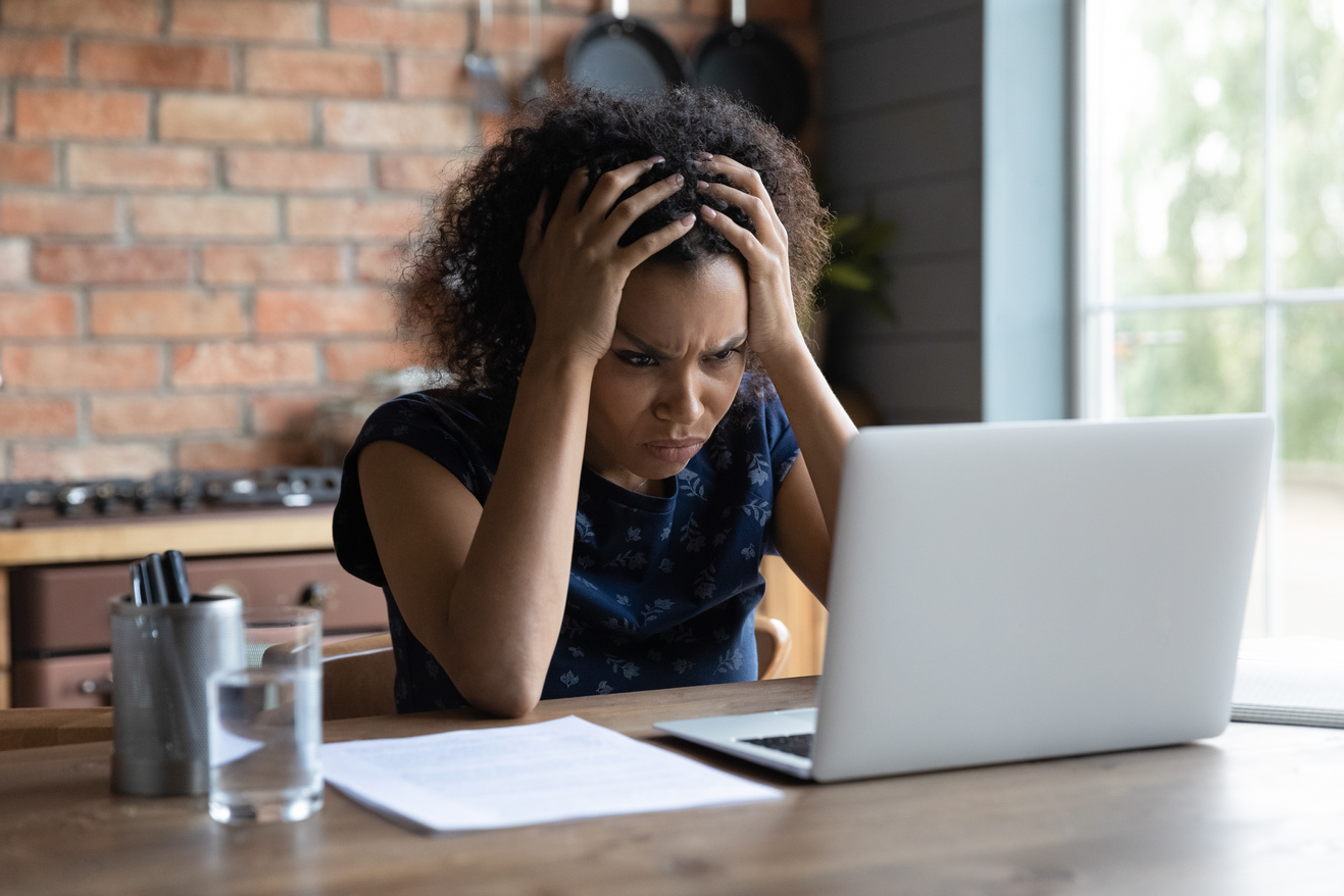 Confused young african ethnicity woman looking at computer screen.